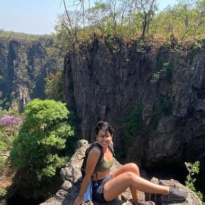 Helô sentada numa pedra diante de um vale verde